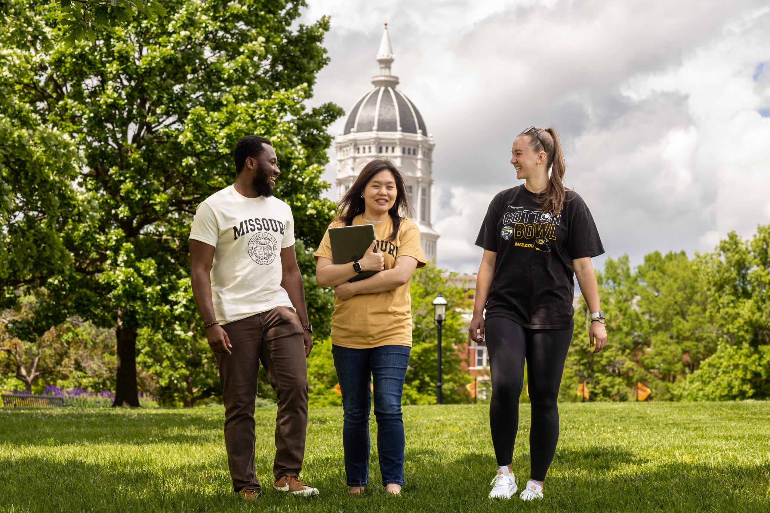 Three students walk outside at the University of Missouri with Jesse Hall showing in the background