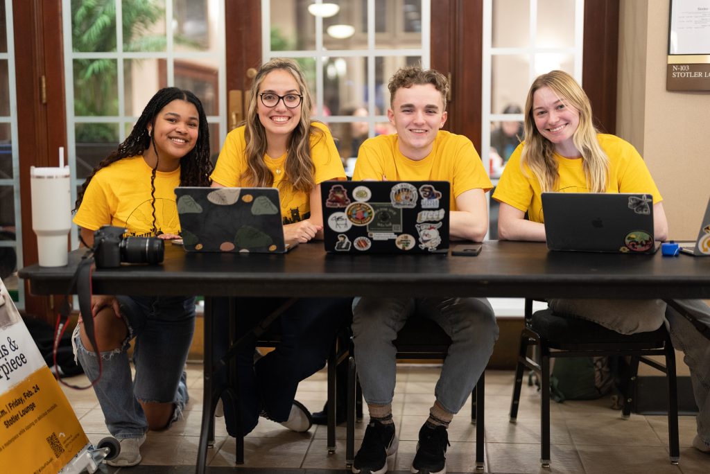 Four students with laptops smiling at the camera
