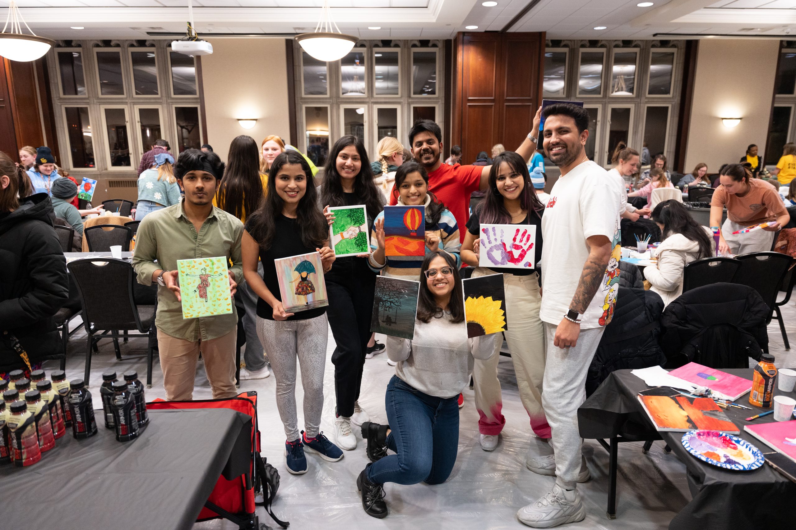A few students hold up drawings and paintings in the Stotler Lounge in Memorial Student Union