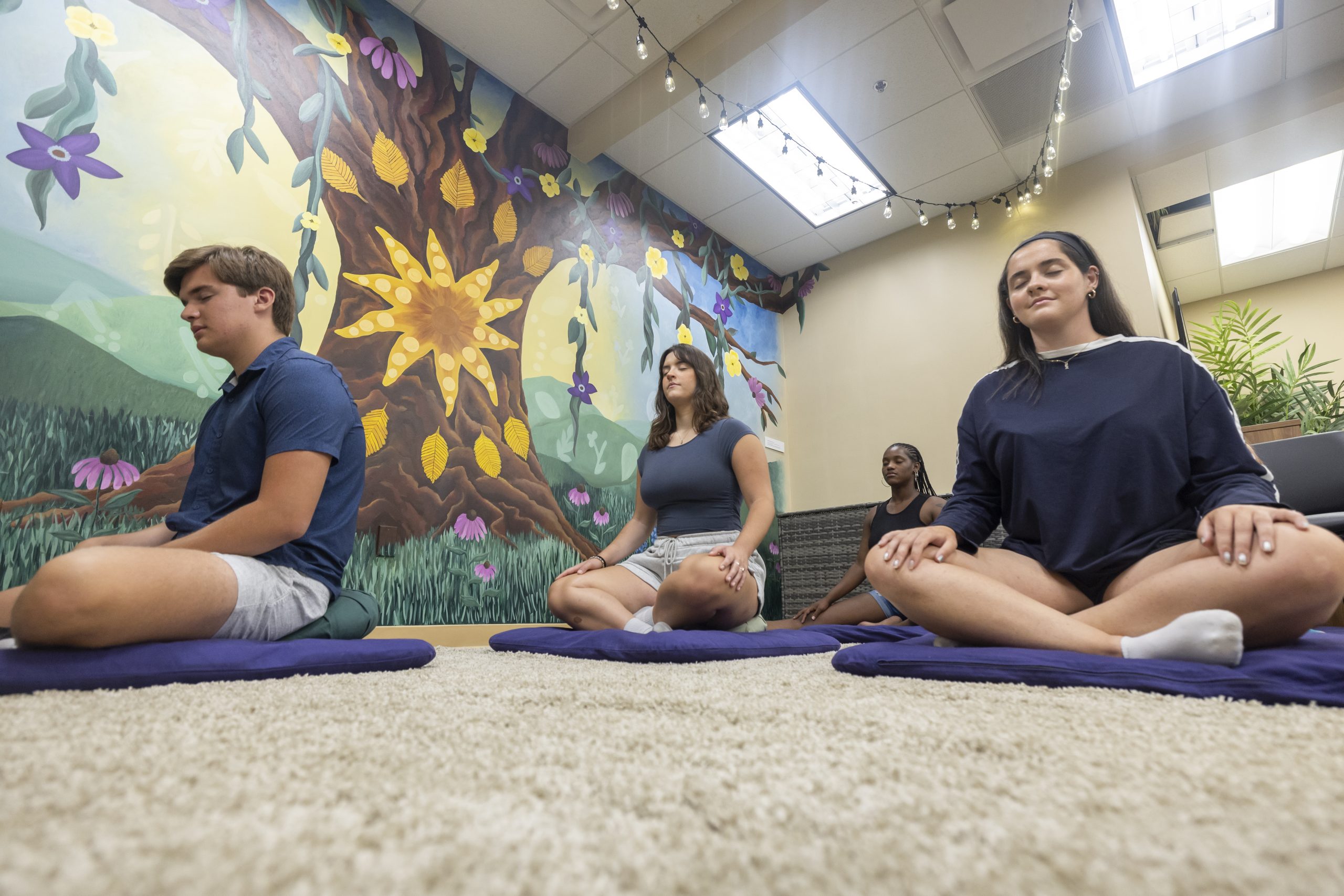 Several students sit cross legged on the floor in meditation in the Wellness Resource Center