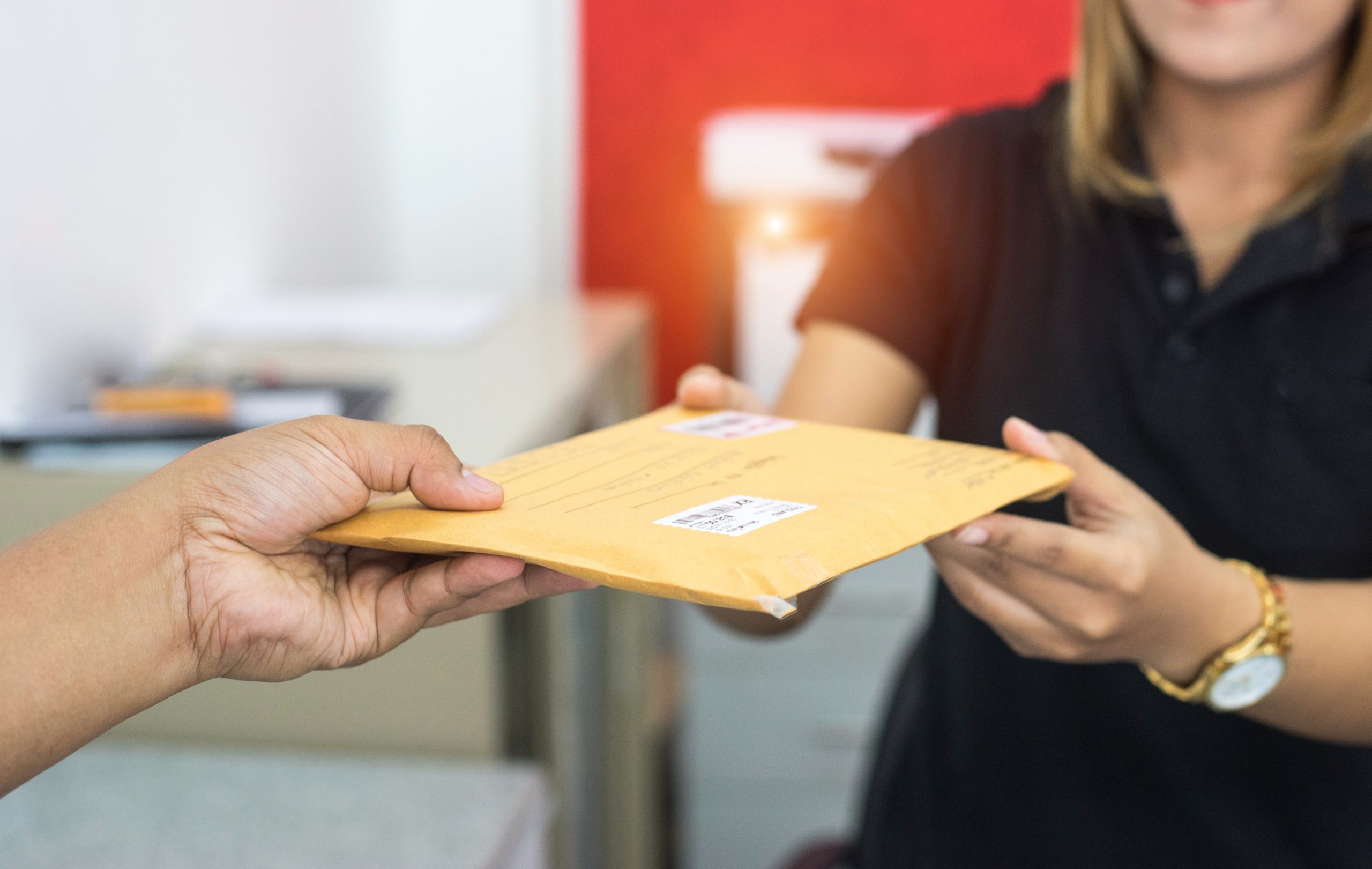 A man handing a mail envelope to a woman