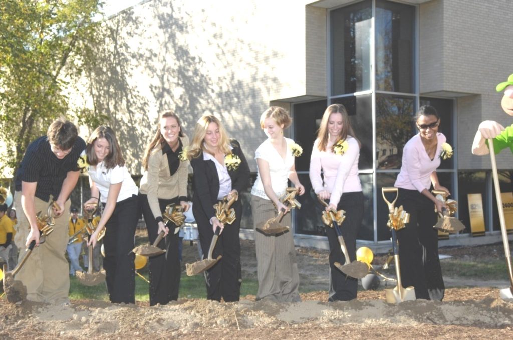A line of people dig shovels in the ground as part of the groundbreaking for the new MU Student Center